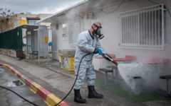 An Israeli firefighter wearing protective clothes disinfects a bus station in the ultra-Orthodox town of Kiryat Ye'arim (Telz-Stone), on March 18, 2020, after seventeen of the city's residents were found to have coronavirus. (Yonatan Sindel/Flash90
