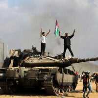 Palestinians wave the national flag and celebrate by a destroyed Israeli tank at the southern Gaza Strip fence east of Khan Younis on October 7, 2023. (AP Photo/Yousef Masoud)