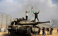 Palestinians wave the national flag and celebrate by a destroyed Israeli tank at the southern Gaza Strip fence east of Khan Younis on October 7, 2023. (AP Photo/Yousef Masoud)