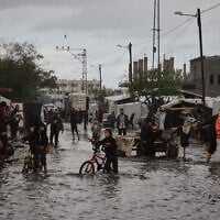 Palestinians walk through a flooded street next to a temporary tent camp after heavy rainfall in Deir al-Balah, central Gaza Strip, Tuesday, Nov. 25, 2025. (AP Photo/Abdel Kareem Hana)