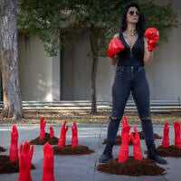 A woman wears punching gloves as mock red hands symbolizing slain women reach out of the ground in a protest display to mark the International Day for the Elimination of Violence against Women, outside Her Academy, a vocational school for survivors of prostitution and abuse, in Tel Aviv. November 24, 2025. (Miriam Alster/Flash90)