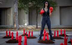 A woman wears punching gloves as mock red hands symbolizing slain women reach out of the ground in a protest display to mark the International Day for the Elimination of Violence against Women, outside Her Academy, a vocational school for survivors of prostitution and abuse, in Tel Aviv. November 24, 2025. (Miriam Alster/Flash90)