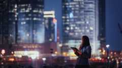 Woman with a laptop, silhouetted against urban buildings