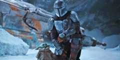 Din Djarin (Pedro Pascal) kneels beside Grogu in the snow on Maldo Kreis in front of the wrecker Razor Crest.