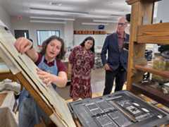 A photo of a librarian showing a historic press to a man and a woman.