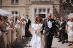 A bride and groom walking outside St Tewdrics whilst guest throw confetti