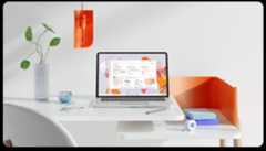 Laptop displaying a productivity application on a white desk with a vase, a notebook, and a pen, with an orange lamp and chair in the background