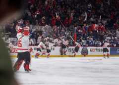 Female hockey players celebrating their win on the ice with the crowd celebrating them in the background.