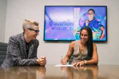 Image of Rafaelle signing a new contract as Haley Carter looks on.