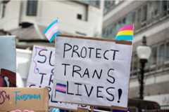 Protect Trans Lives sign with flags and other signs behind