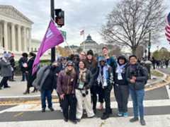 Group photo of members of Advocates for Trans Equality. One person is holding the A4TE flag in the pink color, and the Supreme Court is in the background