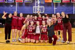 Basketball team and coaches making victory signs with their hand and posing on the court with a trophy.