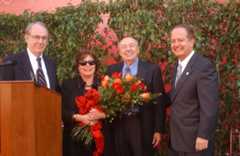 From left to right: USC President Steven Sample, Erna Viterbi, Andrew Viterbi holding a bouquet of flowers, and Engineering School Dean C. L. Max Nikias. They are all standing together outdoors in front of a wall covered with greenery. Erna is wearing sunglasses and holding the bouquet, Andrew is smiling broadly, and both Steven and Max are dressed in suits and ties.