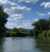 A stunningly beautiful day on the Spokane River, which is framed by lush green trees on either side and crowned with a light blue sky and white puffy clouds.