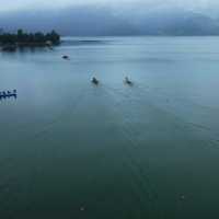 Gray skies appear over a body of water where people float in small boats.