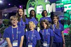 A group of seven people wearing William & Mary iGEM shirts post for a photo next to an iGEM sign.