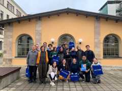A group of students and lecturers are standing in front of an old boiler room, which served as the venue for several schools, with Across bags in their hands.
