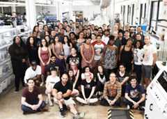 Group photo of approximately 50 people in front of manufacturing equipment