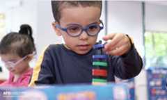 A young boy with a thick-rimmed glasses stares intently at a small ring he is stacking on a toy.