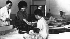 Accompanied by amfAR grantee Dr. Praphan Phanuphak, Elizabeth Taylor greets an AIDS patient in Bangkok, Thailand, in 1989.