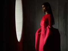 A woman wearing a long red dress stands in an empty room being photographed. The Photo app toggles through the focal lengths to demonstrate the capabilities of the pro camera system, showcasing: 200 mm