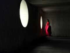 A woman wearing a long red dress stands in an empty room being photographed. The Photo app toggles through the focal lengths to demonstrate the capabilities of the pro camera system, showcasing: 48 mm