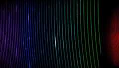 Slightly curved thin luminous lines from purple to turquoise to green to red and then yellow, run vertically over on a black background.