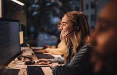 Smiling blond female customer service representative wearing headset using computer at desk in call center