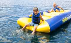 Two young boys sitting on a float in the lake with life vests on