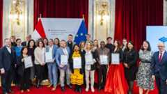 Understanding through Engagement: Presentation of the Intercultural Achievement Awards 2025, Picture: BMEIA/Auer-Grumbach Group photo of recipients of the Intercultural Achievement Award 2025 together with representatives of the Austrian Foreign Ministry. They are standing in front of the flags of Austria and the European Union. The award winners are holding their awards and posing for the photo in a festively decorated room.