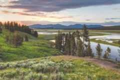 A valley in the mountain range with some trees, hills and a river.
