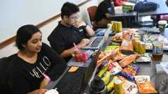 Students code on their laptops at a table overflowing with snacks.