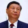 Xi Jinping looking up and to his left against a light gray background.