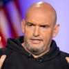 Senator John Fetterman in a dark hoodie speaks and gestures with his hands in the air