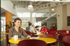 Young woman sat at a table in a social area of a work place