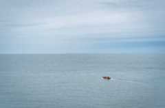 A single boat is travelling on the sea towards the horizon
