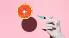 Doctor's hand holding syringe injecting fluid into an orange fruit