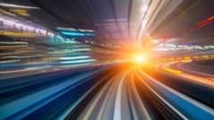 A long-exposure photograph captures a fast-moving train traveling through a brightly lit underground tunnel