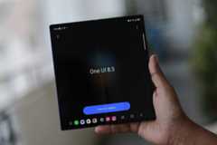 A hand holding a foldable smartphone displaying One UI 8.5 and a Check for updates button on a dark screen.