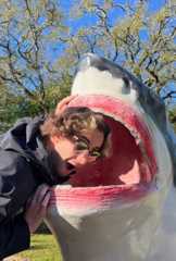 Aidan Hussey student laughing and leaning over to put his head in the mouth of a shark statue 