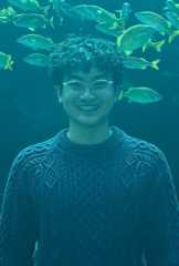 Student Patrick B. Hundley standing in front of large aquarium with many fish