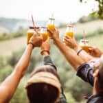 Young happy people on a farm raise bottles of orange juice in a big cheer.