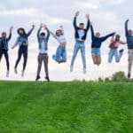 Ten happy friends leaping in the air outdoors.