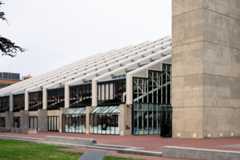 Glass and concrete building with brick patio and grass.
