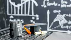 graduation cap and diploma sitting on laptop keyboard with blackboard of charts in the background