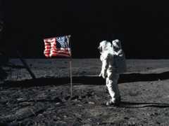 Photo of astronaut Edwin E. Aldrin Jr., lunar module pilot of the first lunar landing mission, poses for a photograph beside the deployed United States flag during an Apollo 11 extravehicular activity (EVA) on the lunar surface. The Lunar Module (LM) is on the left, and the footprints of the astronauts are clearly visible.