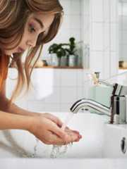 長い茶色の髪の子どもが、白いタイル張りのバスルームの洗面台で手を洗っている。