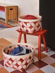 Twee roze/oranje OMMJÄNGE manden met daarin textiel op een geruite vloer naast een rood krukje.