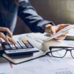 Stressed young woman checking bills, taxes, bank account balance and calculating expenses in the living room at home