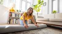 Happy woman moving house and unrolling a carpet while unpacking